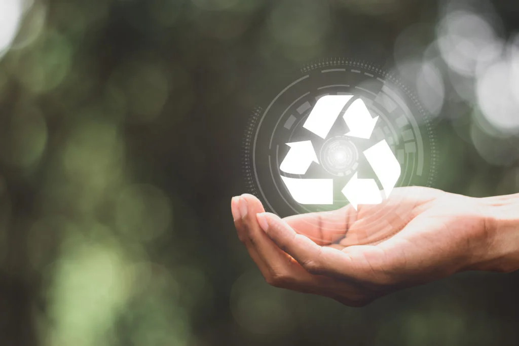 Een open hand houdt een oplichtend recyclingsymbool vast tegen een onscherpe achtergrond van groen.